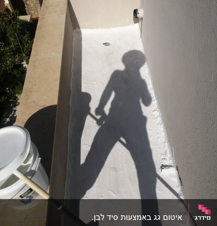 צל של אדם עם מברשת על גג אטום